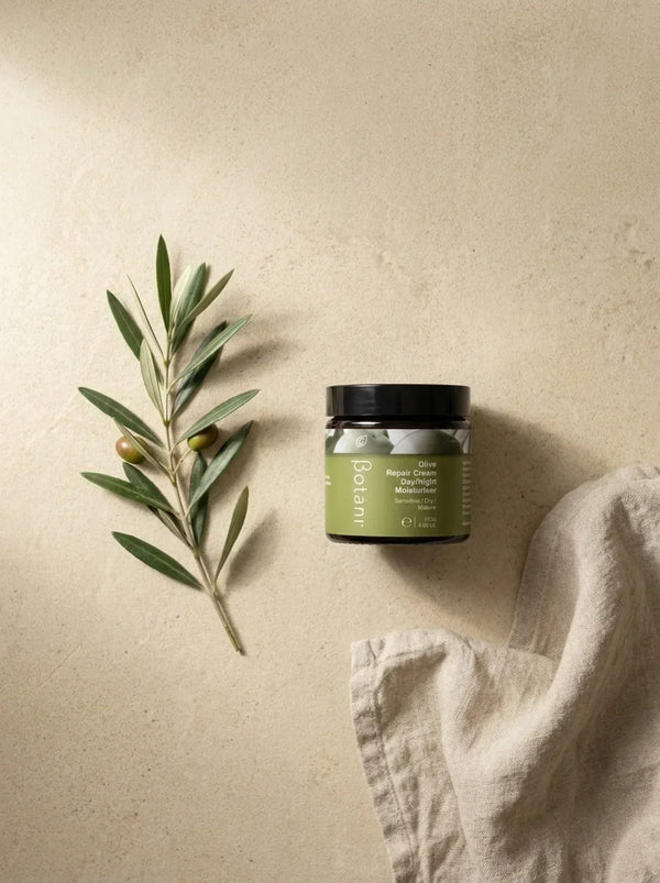 Alt text (for upload): Botani Olive Repair Cream jar closed on a warm cream surface beside a single olive branch and folded linen cloth a quiet, uncluttered skincare routine